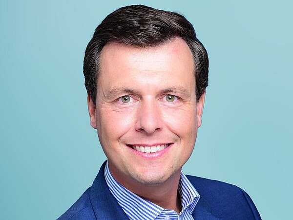 A portrait photo of a man on a light-blue background.