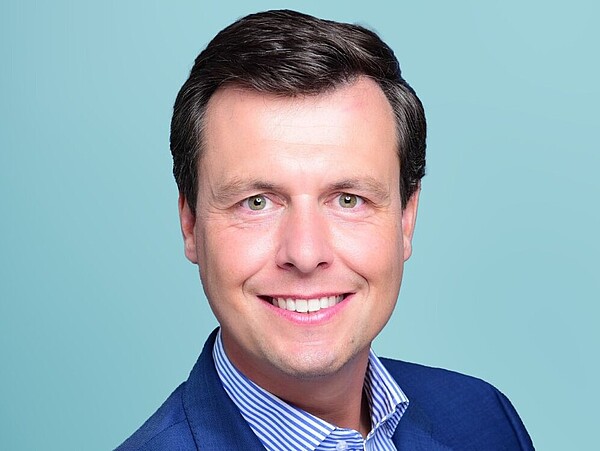 A portrait photo of a man on a light-blue background.